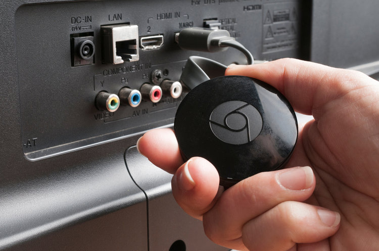a hand holding chromecast connected to tv