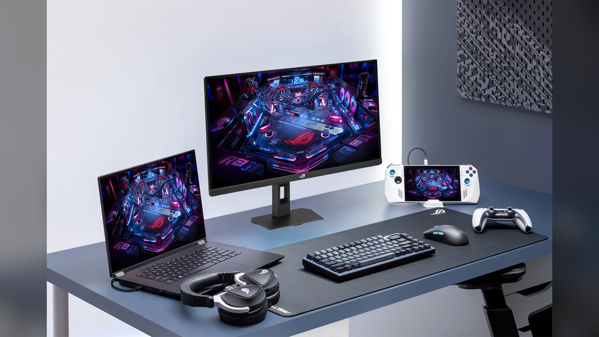 ASUS gaming monitor on a desk with a laptop, keyboard and handheld console