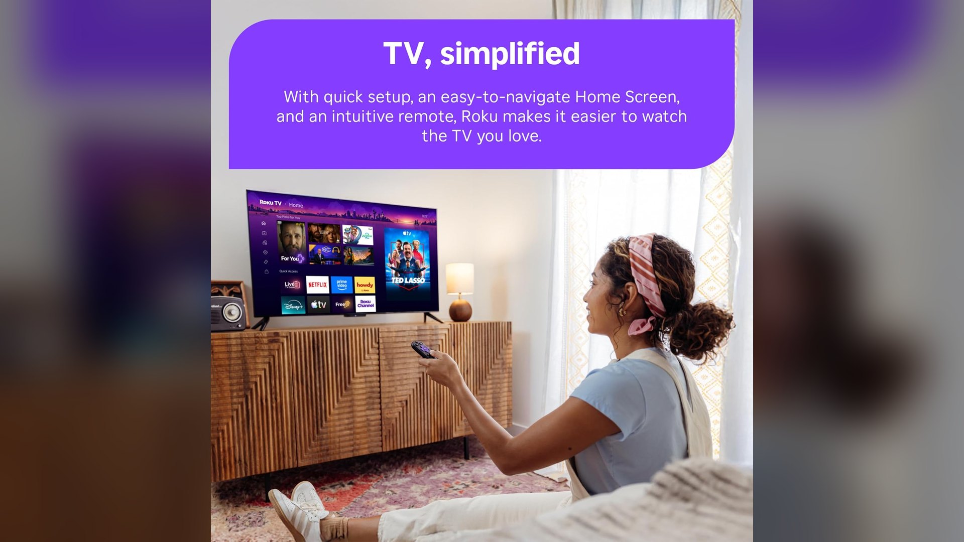 Person pointing a Roku voice remote at a Select Series QLED TV in a living room